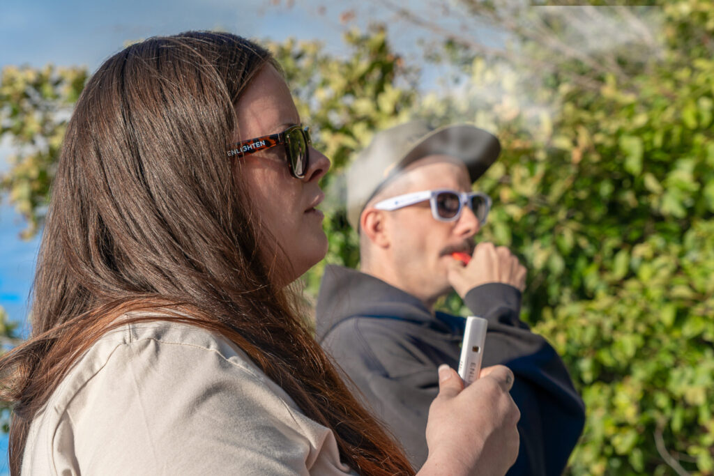 Two people using disposable vape pens wearing Enlighten Alaska's Anchorage dispensary merch
