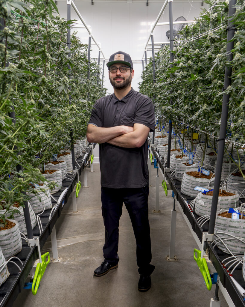 Enlighten Alaska CEO Evan Levinton standing in Enlighten's cannabis cultivation garden facility surrounded by rows of flowering marijuana plants